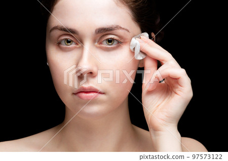 Beautiful girl removes makeup from eyes. Eye-catching. Black background. Close up 97573122