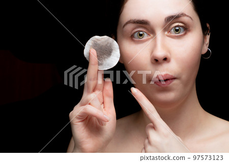 A beautiful girl is surprised and points the finger a cotton pad with makeup. Black background, copy space A beautiful girl is surprised and points the finger a cotton pad with makeup. Black background, copy space 97573123