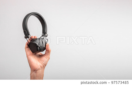 Banner with hand holding wireless headphones. On-air headset. Listening to music, audiobooks concept. Space for text. Banner with hand holding wireless headphones. On-air headset. Listening to music, audiobooks concept. Space for text. 97573485