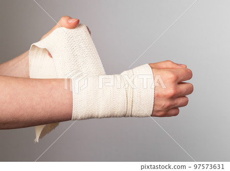 Woman wrapping elastic bandage around painful wrist, forearm. Muscle sprains, strains treatment. Arm injury. Health care concept. Woman wrapping elastic bandage around painful wrist, forearm. Muscle sprains, strains treatment. Arm injury. Health care concept. 97573631