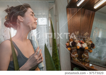 Beautiful girl doing the procedure apparatus Darsonval. Skin care at home 97573820