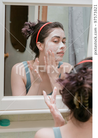 attractive girl uses cosmetics for washing while in the bathroom looking in the mirror 97573821