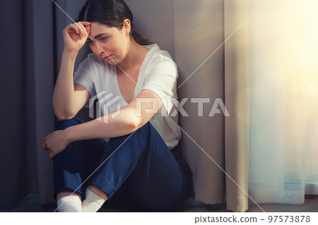Portrait of a stressed crying woman, clutching her head and sitting on the floor. Copy space. Light from window. The concept of domestic violence 97573878