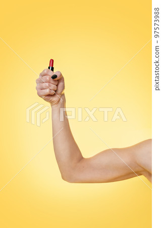 A woman's strong arm shows off her biceps and holds a lipstick. Yellow background. Copy space. Feminism, girl power and the concept of equal rights and independence for women biceps A woman's strong arm shows off her biceps and holds a lipstick. Yellow background. Copy space. Feminism, girl power and the concept of equal rights and independence for women biceps 97573988