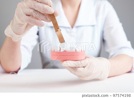 Dentist using forceps for tooth removal from jaw model. Teeth losing concept. Infection, injury consequences. Work of dental surgeon in lab coat and gloves. 97574198