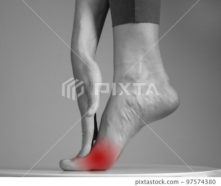Pain in ball of foot. Woman holding leg with red spot closeup. Ache in metatarsal heads. Intense physical activity, inflammation consequences. Health care and medicine concept. Black and white Pain in ball of foot. Woman holding leg with red spot closeup. Ache in metatarsal heads. Intense physical activity, inflammation consequences. Health care and medicine concept. Black and white 97574380