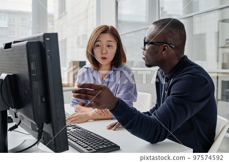 African American programmer pointing at computer monitor and discussing computer program with his colleague African American programmer pointing at computer monitor and discussing computer program with his colleague 97574592