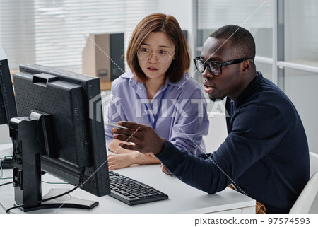 African American programmer pointing at monitor and discussing presentation with his colleague African American programmer pointing at monitor and discussing presentation with his colleague 97574593