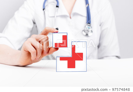First aid. Cubes with red cross in doctor hands. Urgent medical care. Woman in lab coat with stethoscope sitting at table 97574848