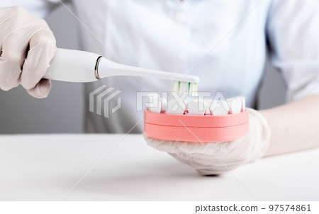 Dentist using electric toothbrush for brushing teeth in jaw model. Cavity, gingivitis and periodontal disease prevention. Stomatology, oral hygiene concept. 97574861