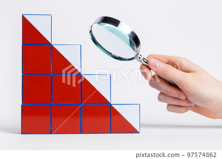 Hand with magnifying glass over falling chart from cubes. Analysis of reasons and consequences of business failure and economic crisis. Search and planning of ways to solve problems 97574862