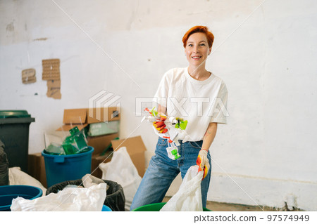Portrait of smiling female worker wearing latex gloves sorting diverse plastic waste for further disposal at modern private waste recycling plant. Concept of environment protection and zero waste 97574949
