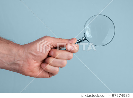 Magnifying glass lens lupe in male hand closeup over blue background 97574985