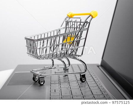Supermarket trolley at laptop keyboard. Online shopping and electronic commerce concept. Buying goods via Internet 97575125