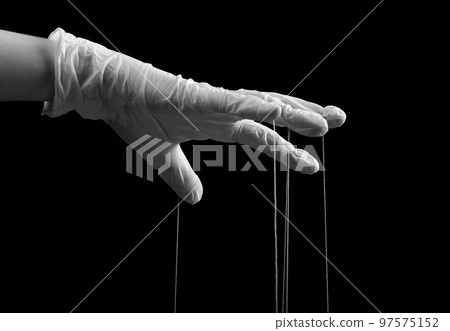 Hand in medical glove with strings on fingers. Fraud, manipulation in medicine, conspiracy theory concept. Black and white. 97575152