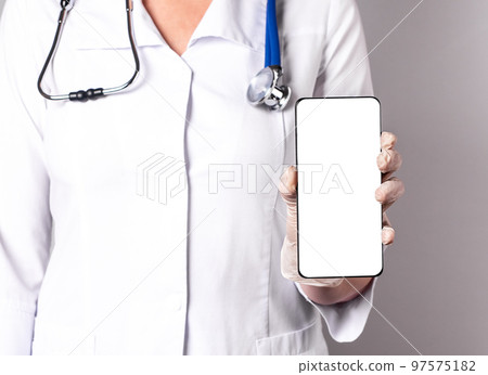 Doctor holding phone with screen mockup. Online medicine, using medical application in smartphone, telehealth, telemedicine concept. Woman in lab coat with stethoscope and gloves 97575182