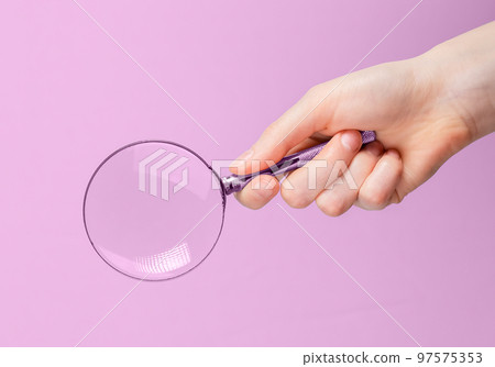 Magnifying glass lens in hand close up over pink background 97575353
