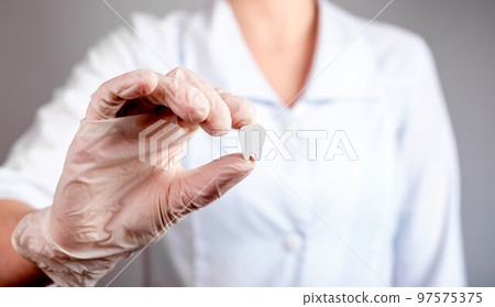 Dentist hand holding white healthy tooth. Implantation, oral hygiene, stomatology, caries and periodontal disease prevention concept. Woman in lab coat and gloves 97575375