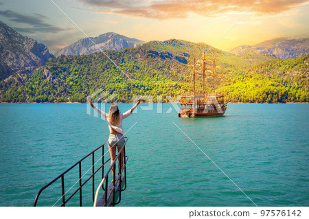 Girl with outstretched hands on bow of boat floating on azure water on sunset 97576142