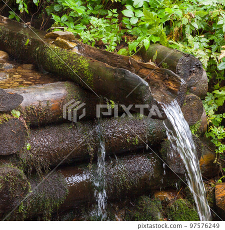 Mountain brook. Wooden log well. Mountain brook. Wooden log well. 97576249