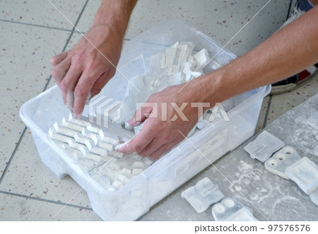 Male worker sorts through models in hands, lying in box and covered with white polyamide powder close-up. Objects printed on powder 3D printer. Technology Multi Jet Fusion MJF. 3D printing technology Male worker sorts through models in hands, lying in box and covered with white polyamide powder close-up. Objects printed on powder 3D printer. Technology Multi Jet Fusion MJF. 3D printing technology 97576576