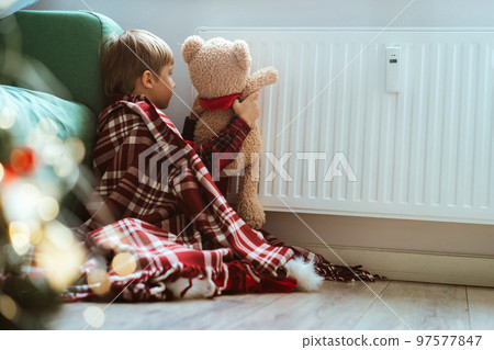 cute little boy wrapped id plaid sitting by heater warming teddy bear paws 97577847