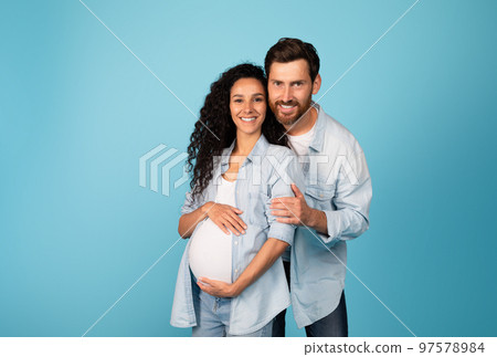 Smiling young european male hugging pregnant female in casual with big belly, isolated on blue background Smiling young european male hugging pregnant female in casual with big belly, isolated on blue background 97578984
