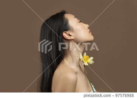 Profile shot of korean lady posing with daffodil flower over brown background, attractive woman with smooth skin Profile shot of korean lady posing with daffodil flower over brown background, attractive woman with smooth skin 97578988