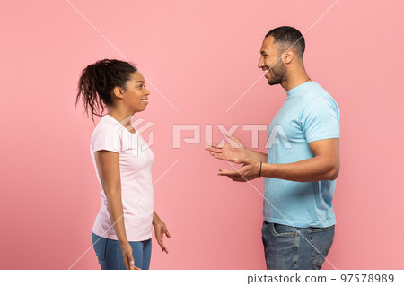 Side view of excited african american friends man and woman spreading hands and talking, pink background Side view of excited african american friends man and woman spreading hands and talking, pink background 97578989