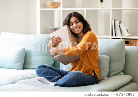 Arab Woman Embracing Big Cardboard Box While Sitting On Couch At Home 97578998