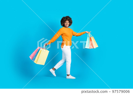 Positive carefree black woman shopaholic walking with purchases 97579006
