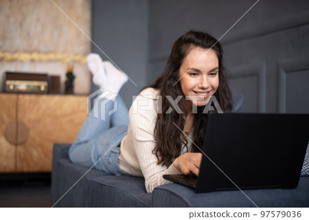 Happy caucasian woman using laptop pc computer, working or studying online, lying on sofa at home, free space Happy caucasian woman using laptop pc computer, working or studying online, lying on sofa at home, free space 97579036