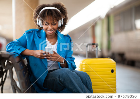 Happy Young Black Woman Messaging On Smartphone While Sitting At Railway Station 97579050