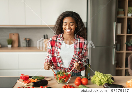 Satisfied glad millennial black female preparing salad at table with organic vegetables, has fun at spare time 97579157
