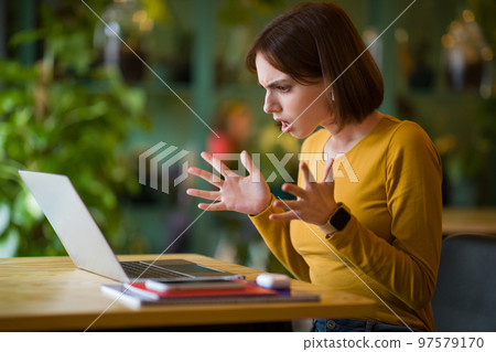 Angry young woman sitting in cafe, working online on laptop Angry young woman sitting in cafe, working online on laptop 97579170