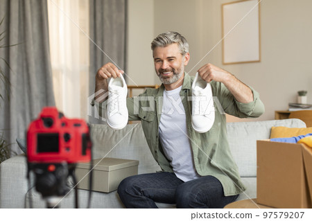 Glad old caucasian man shopaholic blogger shoots video blog on camera with blank screen shows shoes 97579207