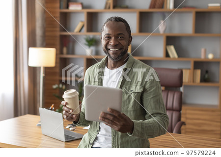 Cheerful handsome mature black businessman with tablet and cup of drink takeaway watch at camera Cheerful handsome mature black businessman with tablet and cup of drink takeaway watch at camera 97579224