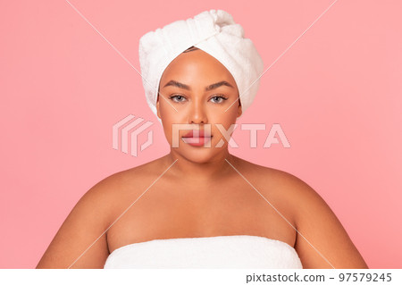 Portrait of body positive african american lady wearing towel, standing over pink studio background Portrait of body positive african american lady wearing towel, standing over pink studio background 97579245