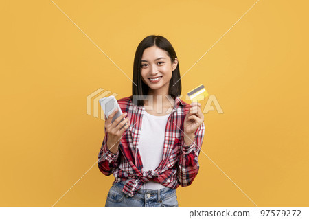 Easy money transfer. Happy young asian lady holding debit credit card and using mobile phone, making online payment 97579272