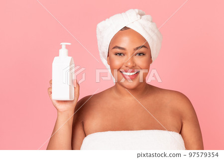 Attractive african american plus size lady with bottle of moisturising body lotion, posing over pink background 97579354