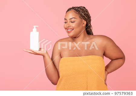 Beautiful black oversize woman holding bottle with body lotion, recommending new skincare product 97579363