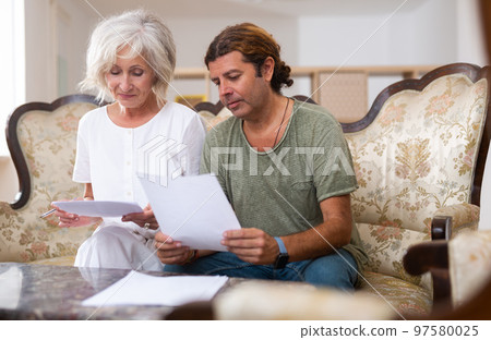 Aged woman and man sign documents sitting in room interior 97580025