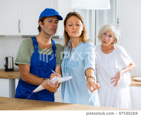Housewife tells the plumber where to change the pipes in the kitchen Housewife tells the plumber where to change the pipes in the kitchen 97580269