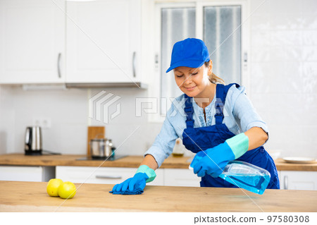 Professional female cleaner in uniform using spray chemistry on the kitchen countertop Professional female cleaner in uniform using spray chemistry on the kitchen countertop 97580308