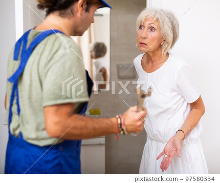 Elderly woman talking with plumber at home Elderly woman talking with plumber at home 97580334