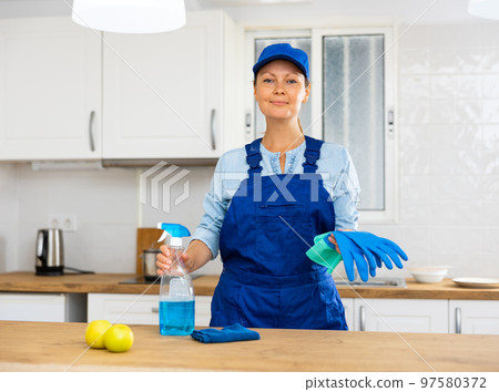 Skilled woman house cleaner sanitizing kitchen countertop 97580372