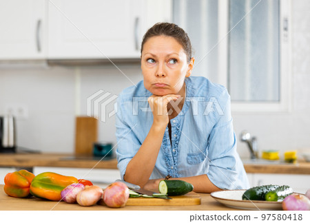 Sad young adult woman standing in kitchen 97580418