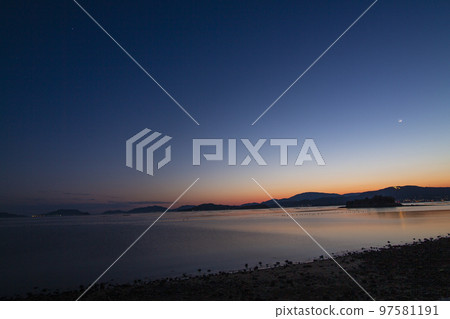 The sun sets over the Seto Inland Sea with a crescent moon and a bonfire The sun sets over the Seto Inland Sea with a crescent moon and a bonfire 97581191