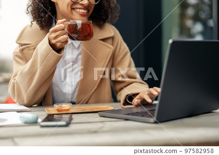 Afro american woman freelancer working remotely and drinking tea while sitting on cafe terrace 97582958