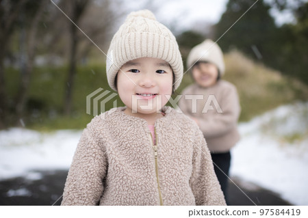 Girl sisters wearing knitted hats playing in the snow in winter Girl sisters wearing knitted hats playing in the snow in winter 97584419